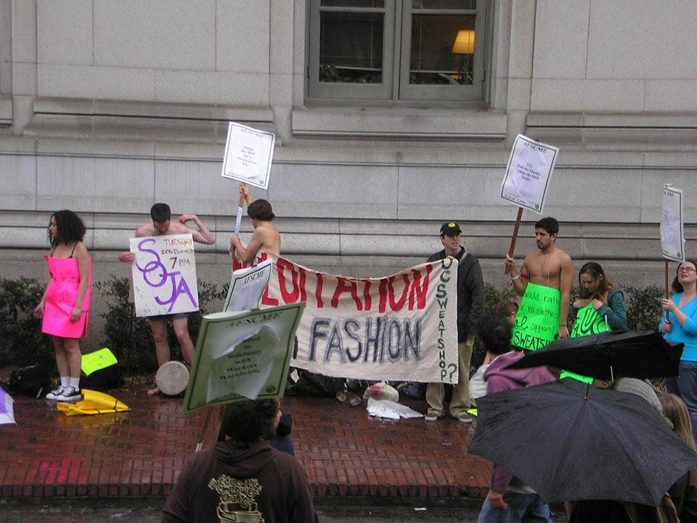 A group of students stage a protest. They are holding signs and a number of them are wearing no shirts or have only their signs covering their bodies.