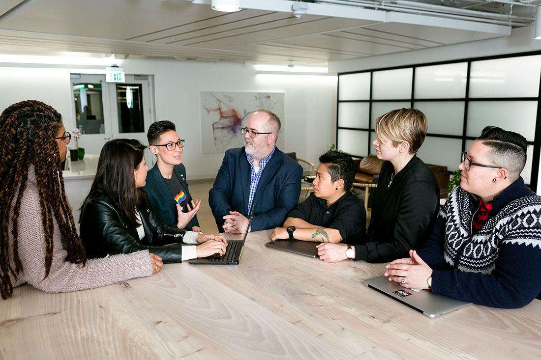 Seven people stand around a conference room table.