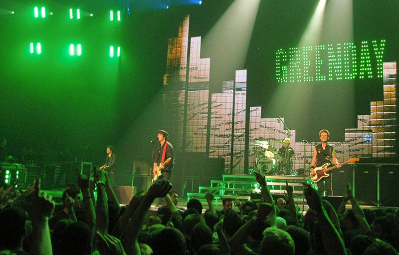 Band performing on a large stage with a cheering crowd in the foreground.