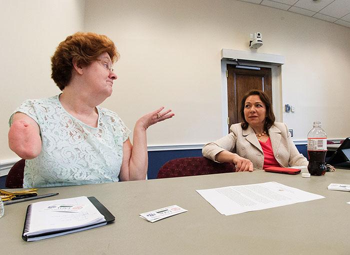 Two people sit at a conference room table and appear to be in a conversation.