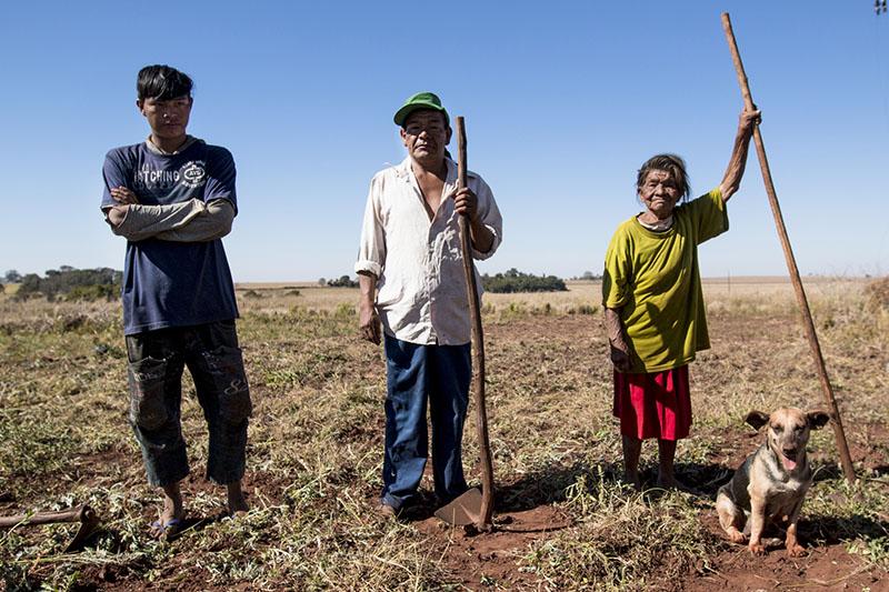 Three people with a small dog stand in an open field.