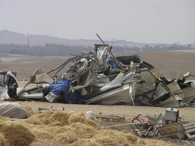 A woman standing in front of a twisted pile of metal sheeting that once was a house.