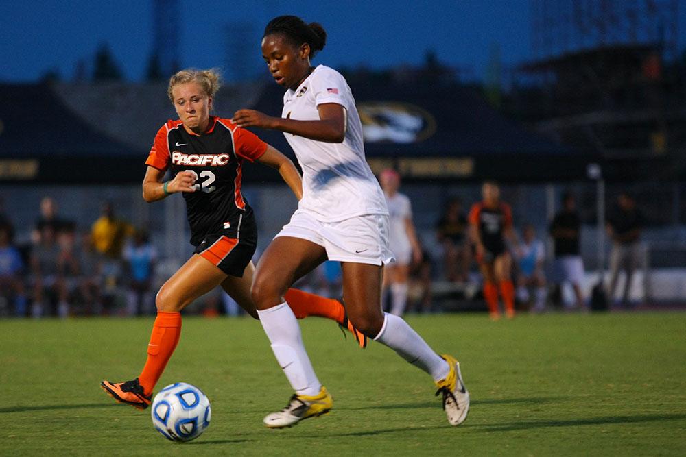 A soccer player dribbles the ball while a member of the other team approaches.