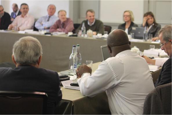 A photograph shows a group of people seated around tables in a meeting room.