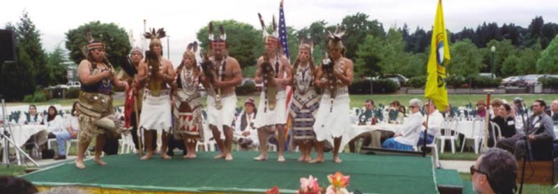 Eight dancers in traditional attire perform on a stage.