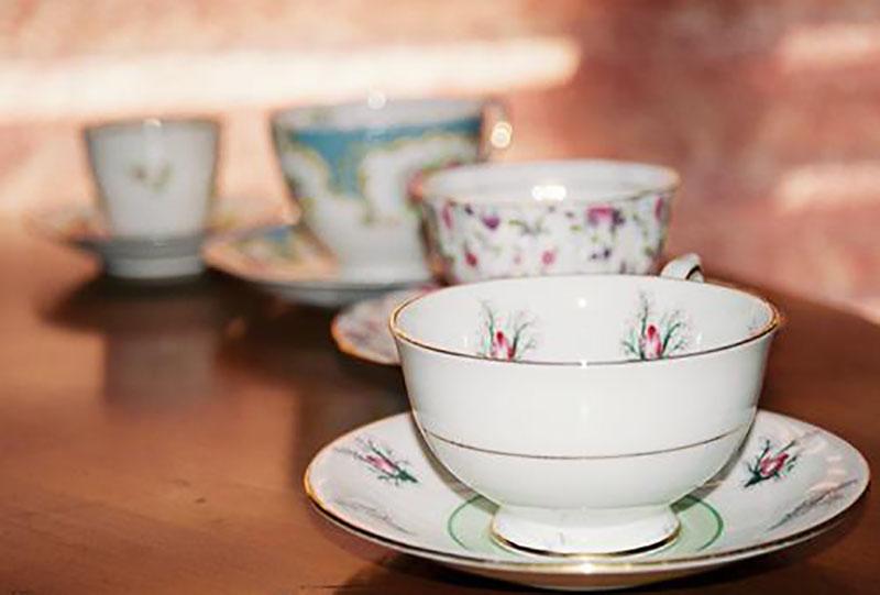 Four porcelain teacups with saucers lined up on a table.