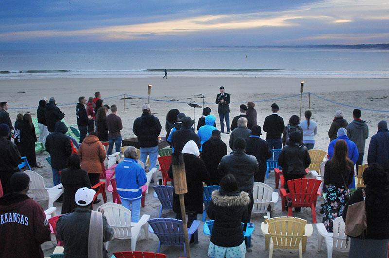 A group of people standing on a beach at sunrise. One person stands facing the group.