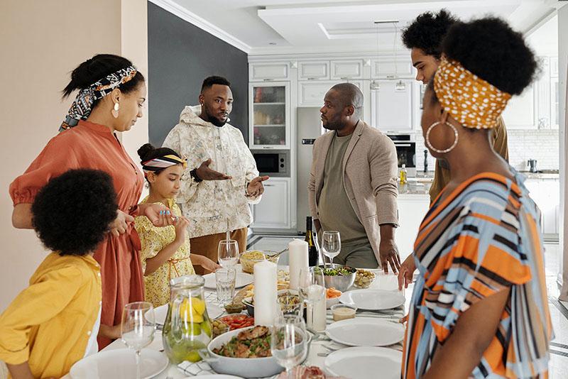 A group of people stand around a table with food on it.