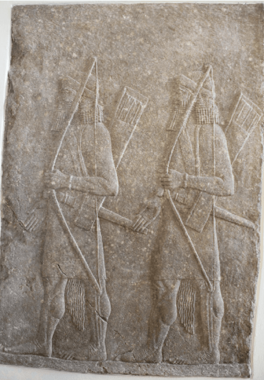 A picture of a stone carving of two almost identical figures is shown on gray stone. Both figures are facing left, wearing rounded helmets with long hair and beards, cloths tied with long sashes around their waists, and barefoot. Both figures carry bows in their left hands, axes at their waists, and quivers on their backs.