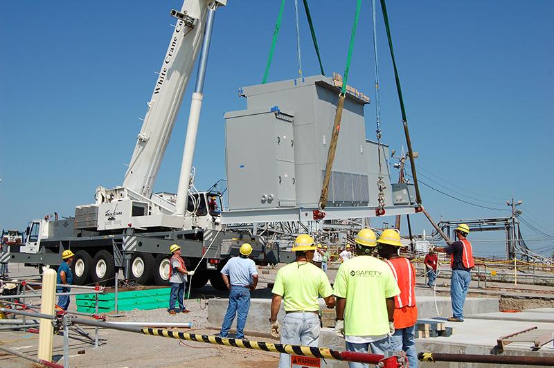 Construction site with workers wearing safety helmets and bright orange vests.