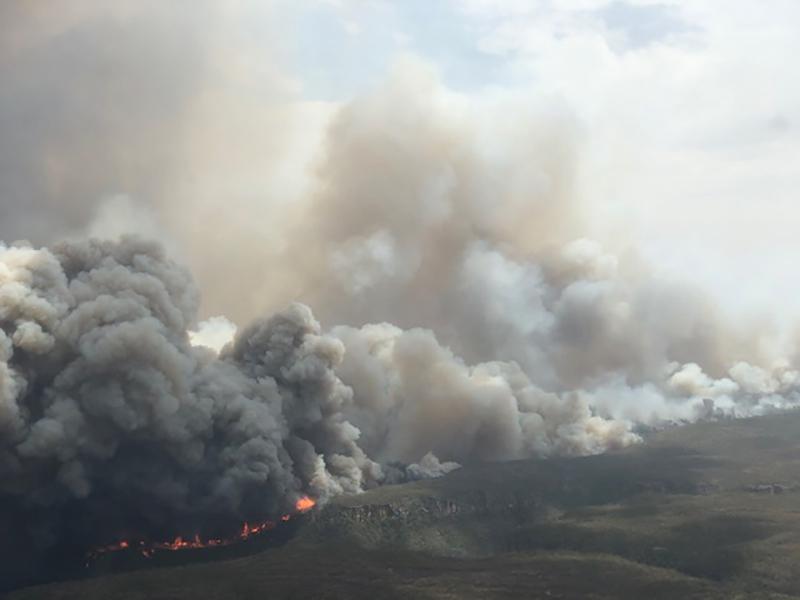 Distant view of the landscape with enormous clouds of smoke rising from fires burning on the ground.