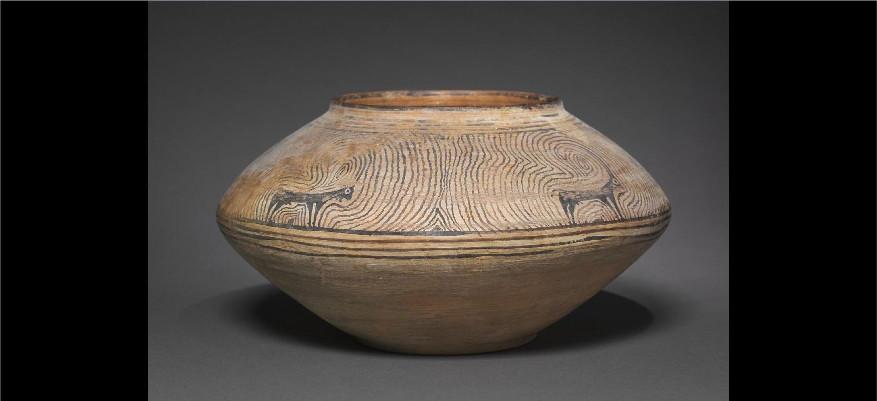 An image of an ancient piece of pottery is shown on a gray background. The item is beige, short, has a round opening at the top, and a thicker middle than the top and bottom. The top is decorated with two black animals with four legs and large white eyes. The horns on top of the head are long and turn into black swirls that cover the top of the item. Four horizonal stripes show in the middle and the lower half of the item is beige with black highlights.