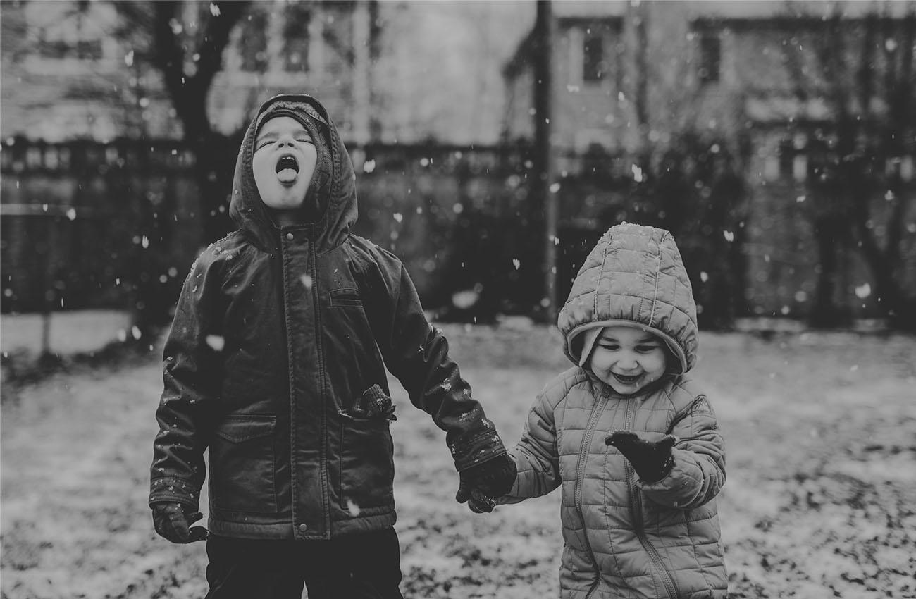 A photograph shows two children holding hands and catching snowflakes with their tongues.