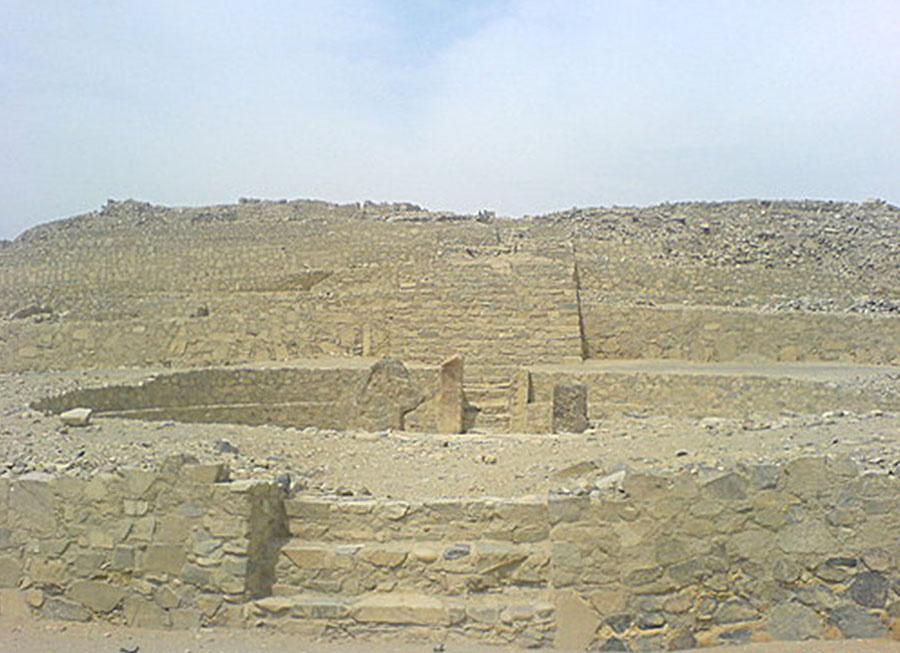 A picture is shown of a drab, flat landscape with barren mountains in the background. In the forefront there are three square stone ruins in a pyramid shape, with the tops missing. The ruins show staircases in the middle.