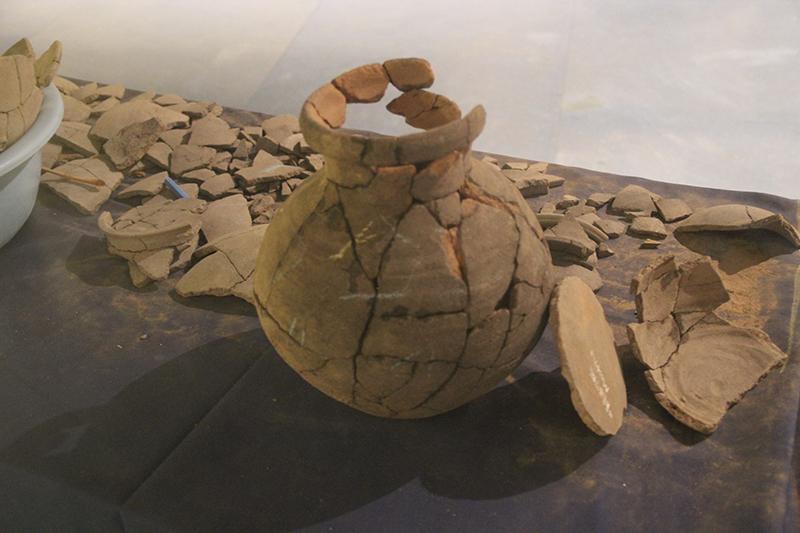 Pottery shards - some laid out on a table and others fitted together to form most of a vase.