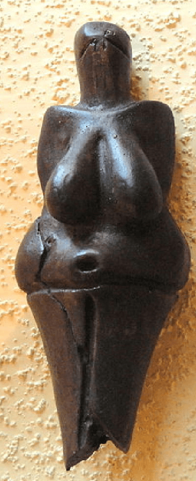 A picture of a black sculpture is shown on a yellow bumpy background. The sculpture has a long, rectangularly rounded head with two slits toward the top. Broad shoulders lead to large hanging breasts and a large belly extending on both sides with a deep belly button in the middle. The bottom is one triangular piece with a jagged bottom. A large crack runs along the left side from the bottom to the belly.