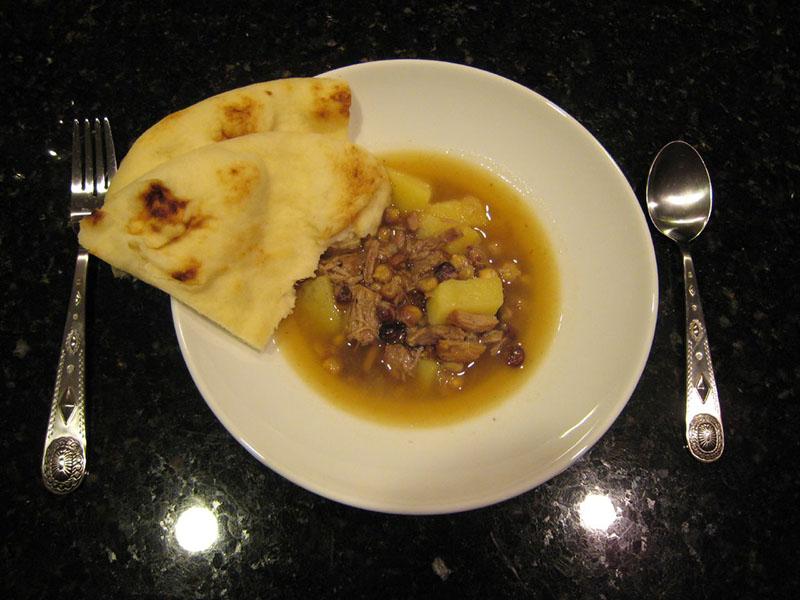 A bowl of Navajo mutton stew with blue corn. A piece of flat bread is on the side of the bowl.